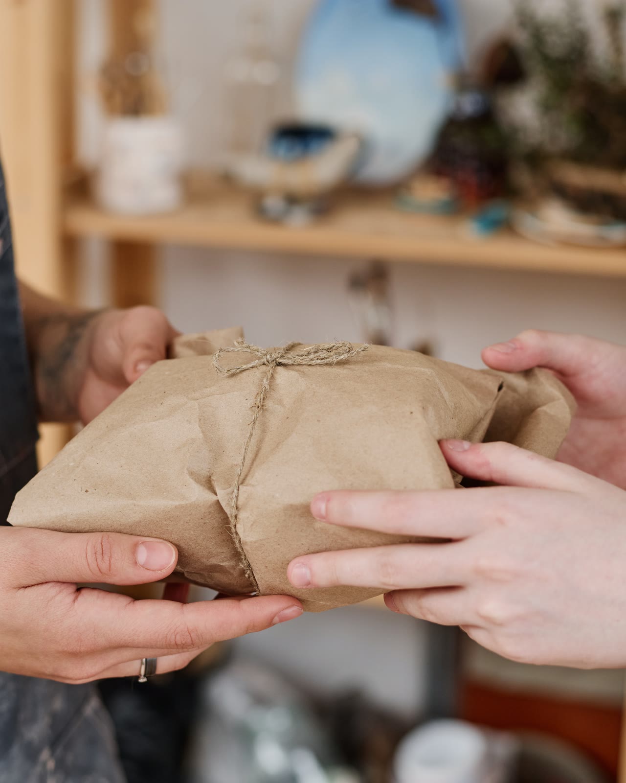 A potter's clay-marked hands passing a paper-wrapped parcel to a customer.