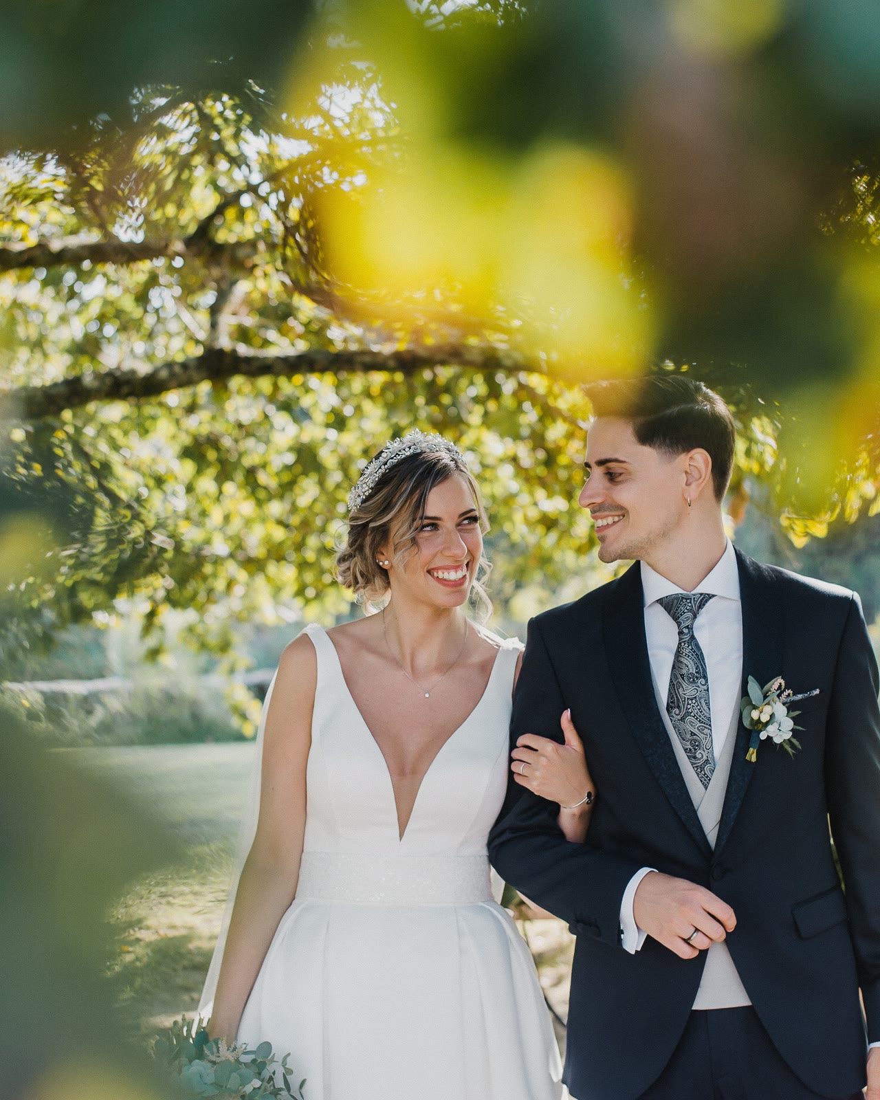 A couple walking arm in arm under a tree in warm afternoon sun.