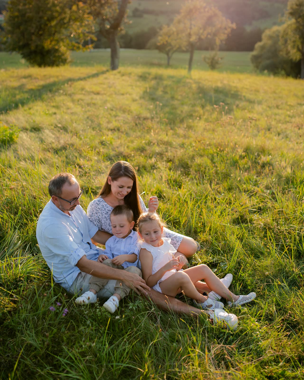 A family of four sitting on a sloping meadow under fruit trees as the sun drops behind the ridge.